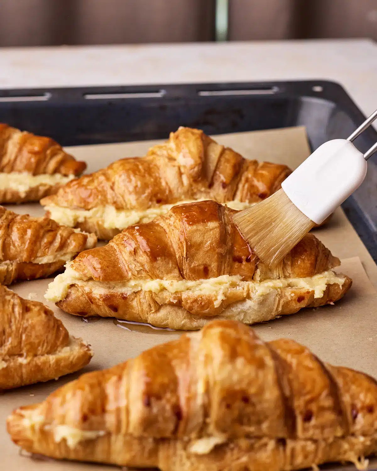 Brushing simple syrup on top of almond croissants before baking.
