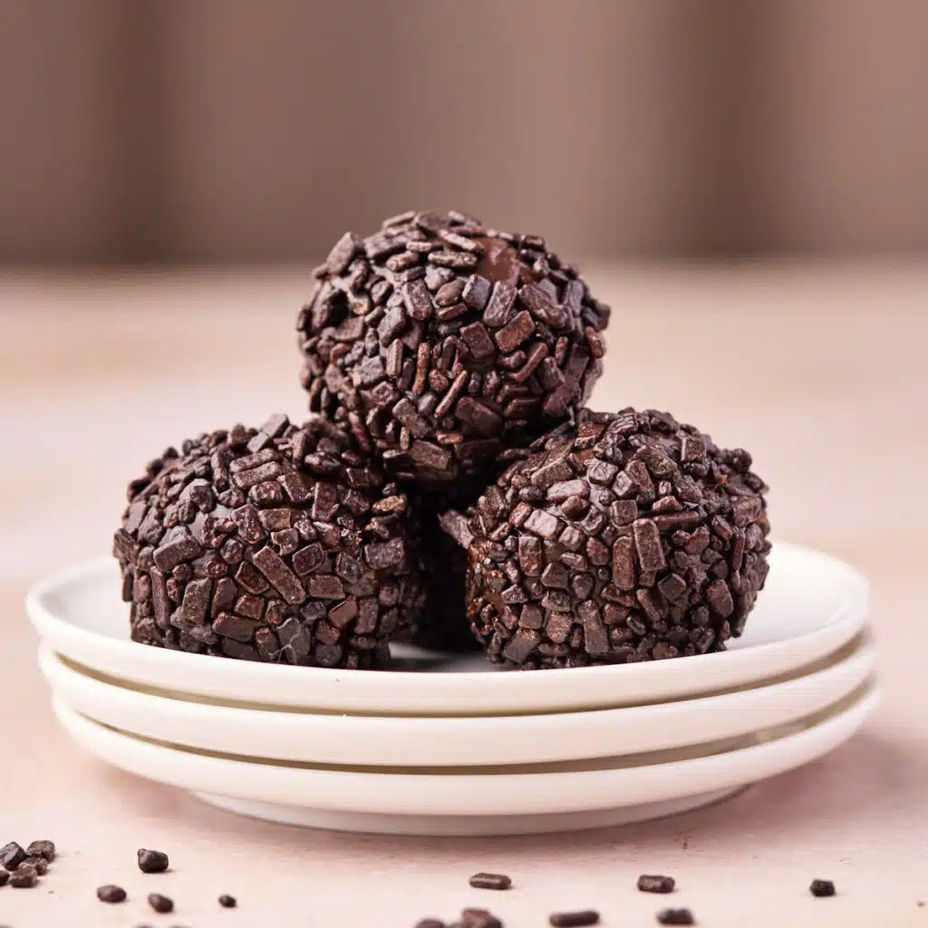 Three brigadeiro piled on top of tiny plates, covered in chocolate sprinkles.