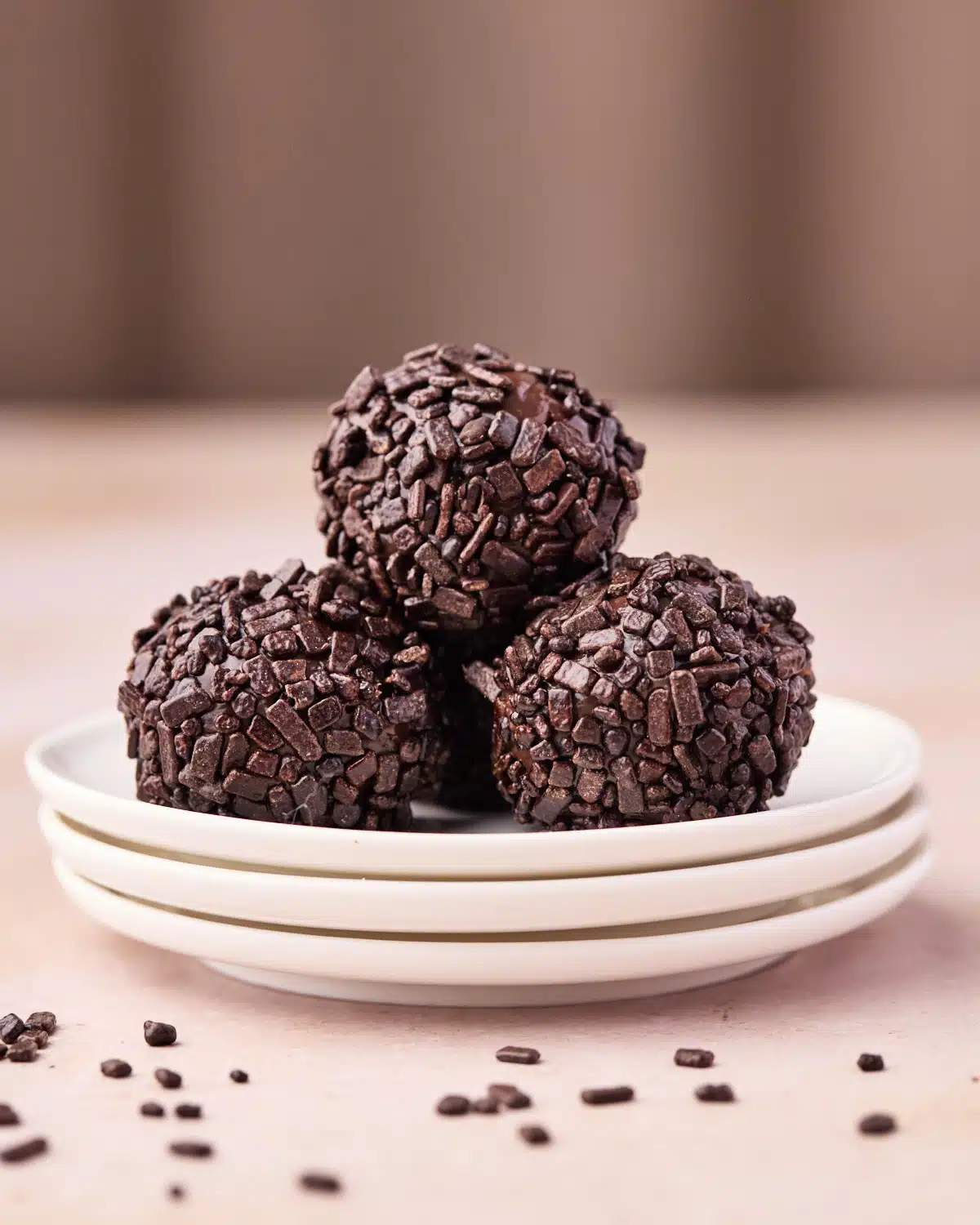 Three brigadeiro piled on top of tiny plates, covered in chocolate sprinkles.