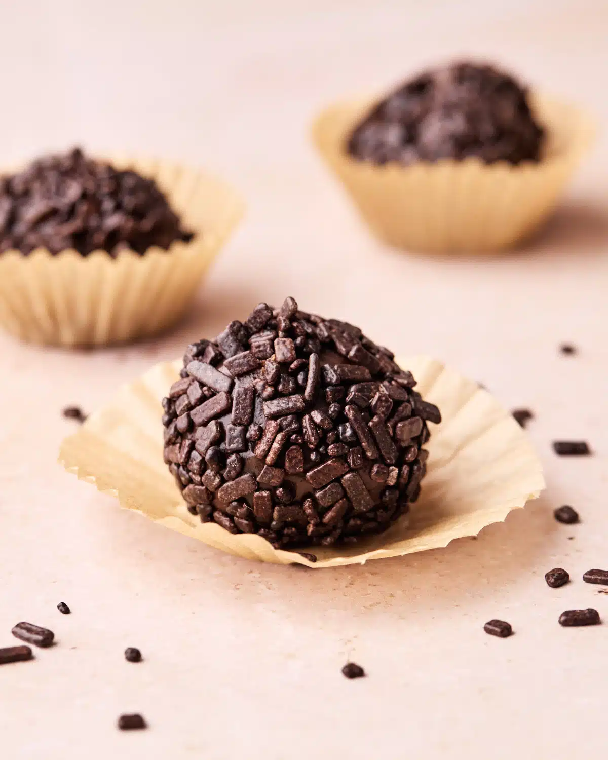 Three brigadeiro on a table, one is out of the paper case.