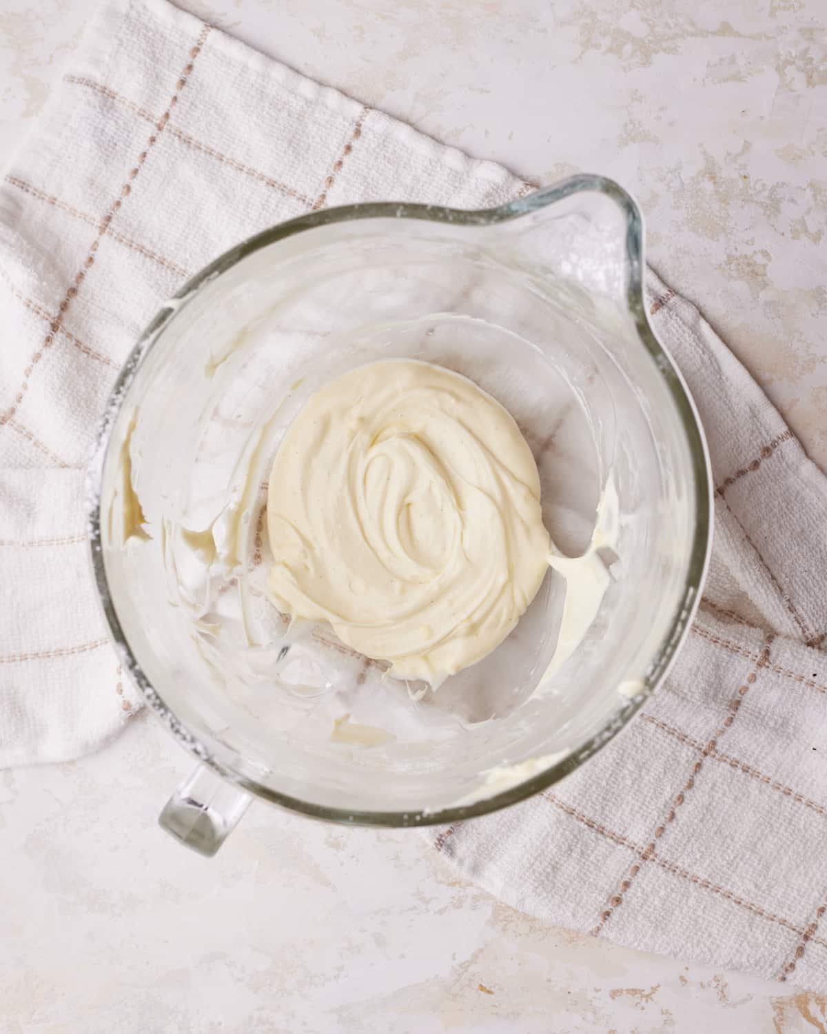 Cream cheese glaze in a glass bowl, sitting on a tea towel.