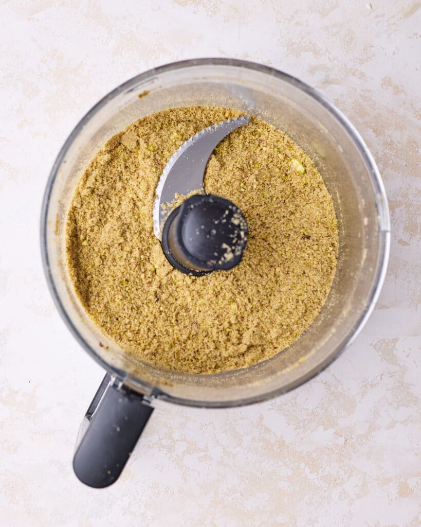 Combining graham crackers with pistachios in a food processor to make a pistachio graham cracker crust for cheesecake. 