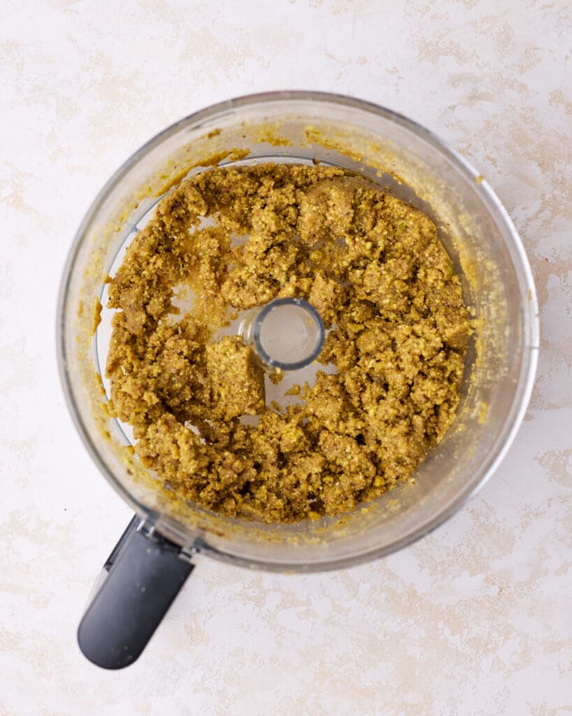 Pistachio graham cracker crust mixture in a food processor, ready to be used. 