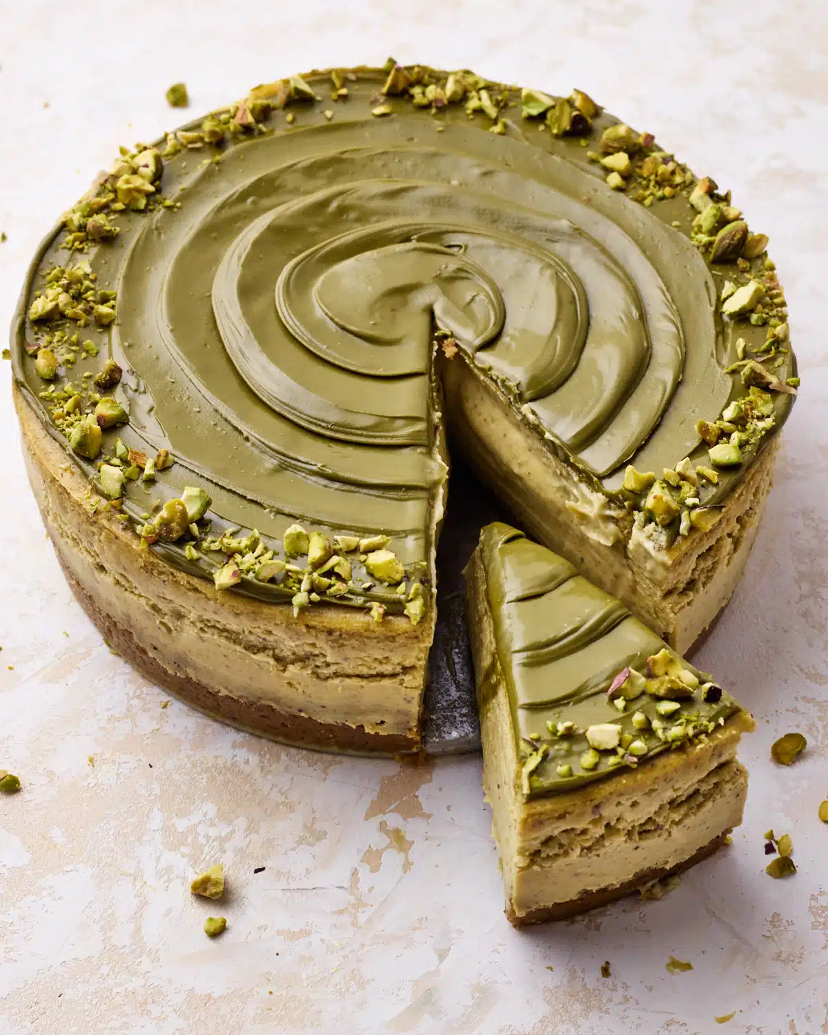 Pistachio cheesecake decorated with a swirl of pistachio cream and chopped pistachios around the outside, with a slice being taken out of it.