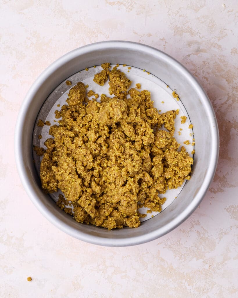 Pistachio graham cracker crust mixture in a cheesecake pan. 