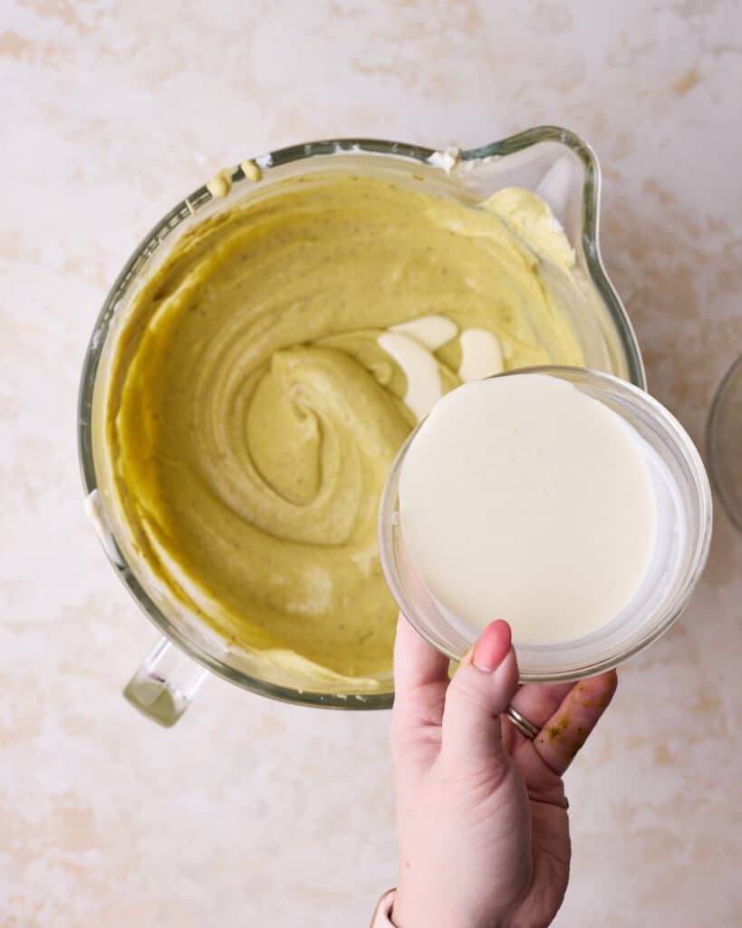 Gradually drizzling cream into pistachio cheesecake batter. 