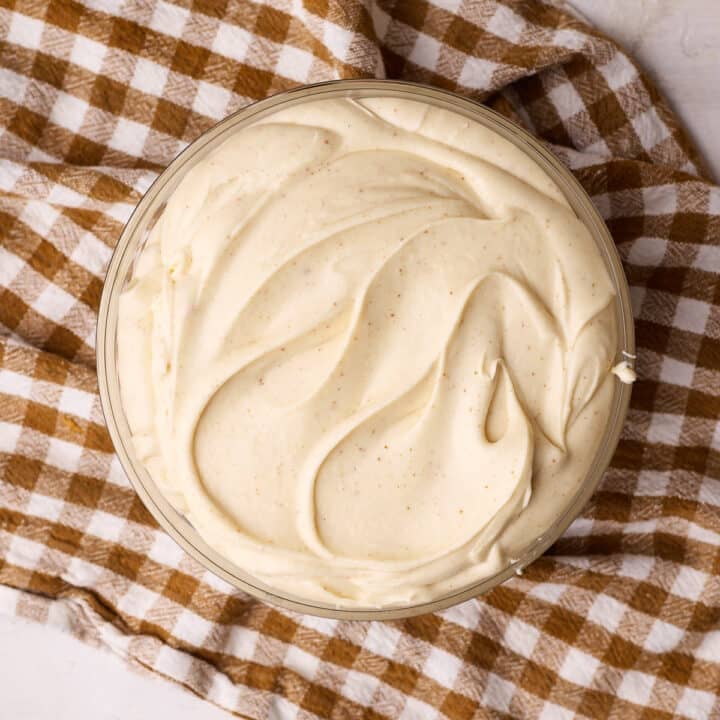 Brown butter cream cheese frosting in a glass bowl on top of a brown chequered tea towel.