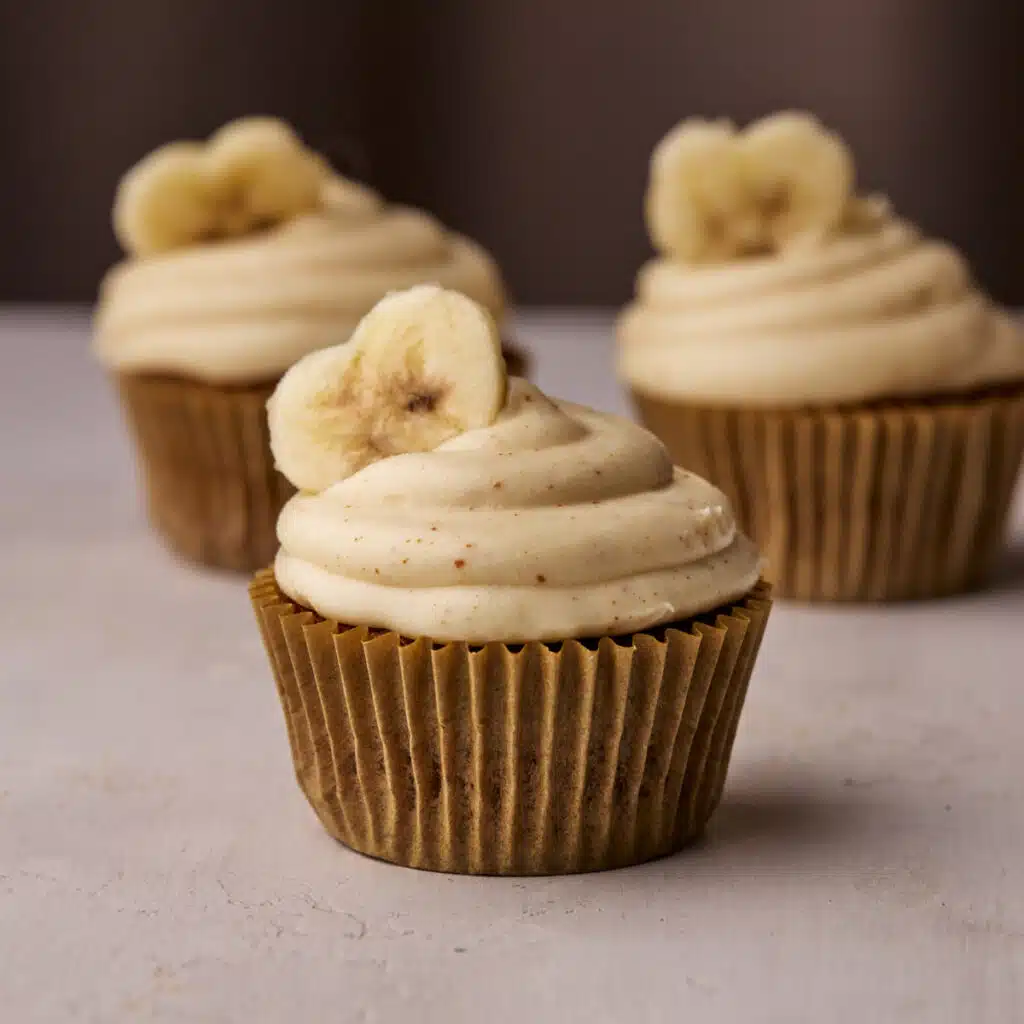 Three banana cupcakes with brown butter cream cheese frosting and a heart shaped banana slice on top.