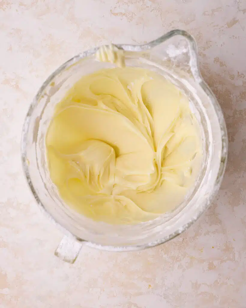 cream cheese and butter being beaten together in a glass bowl to make cream cheese frosting. 