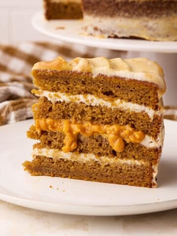 Slice of pumpkin cake showing layers of cinnamon cream cheese frosting and pumpkin curd.