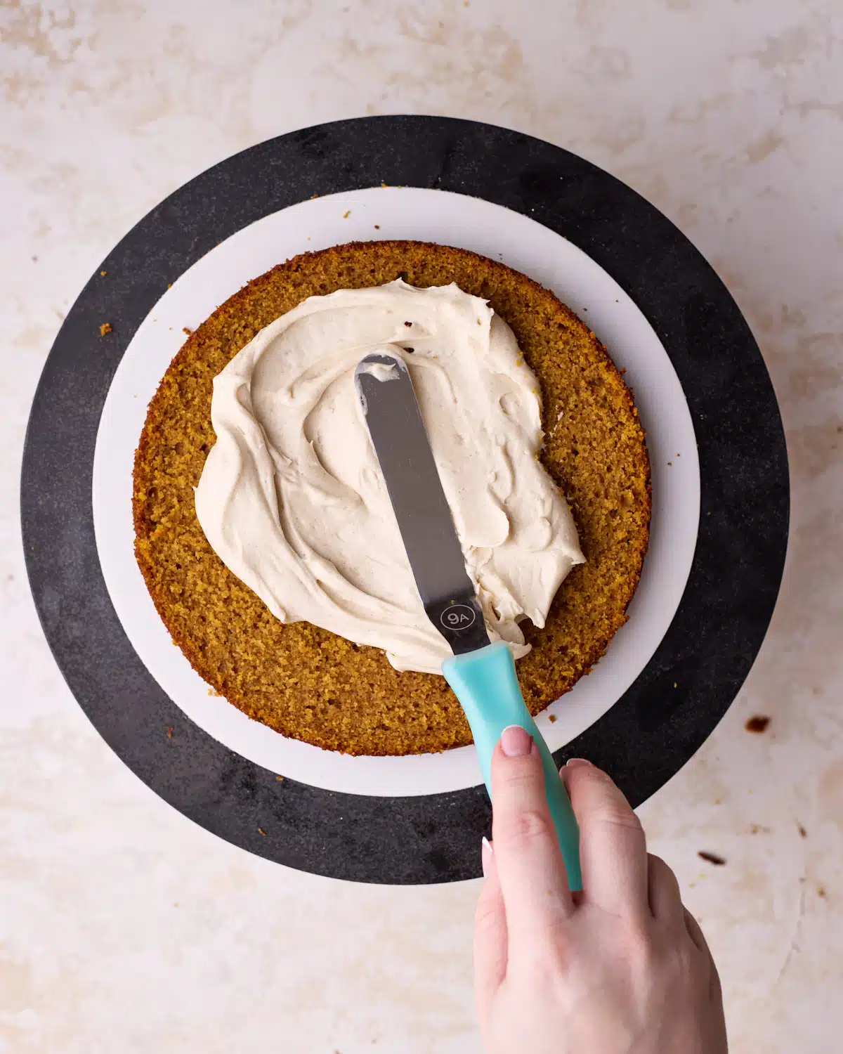 Spreading cinnamon cream cheese frosting onto a layer of pumpkin cake.
