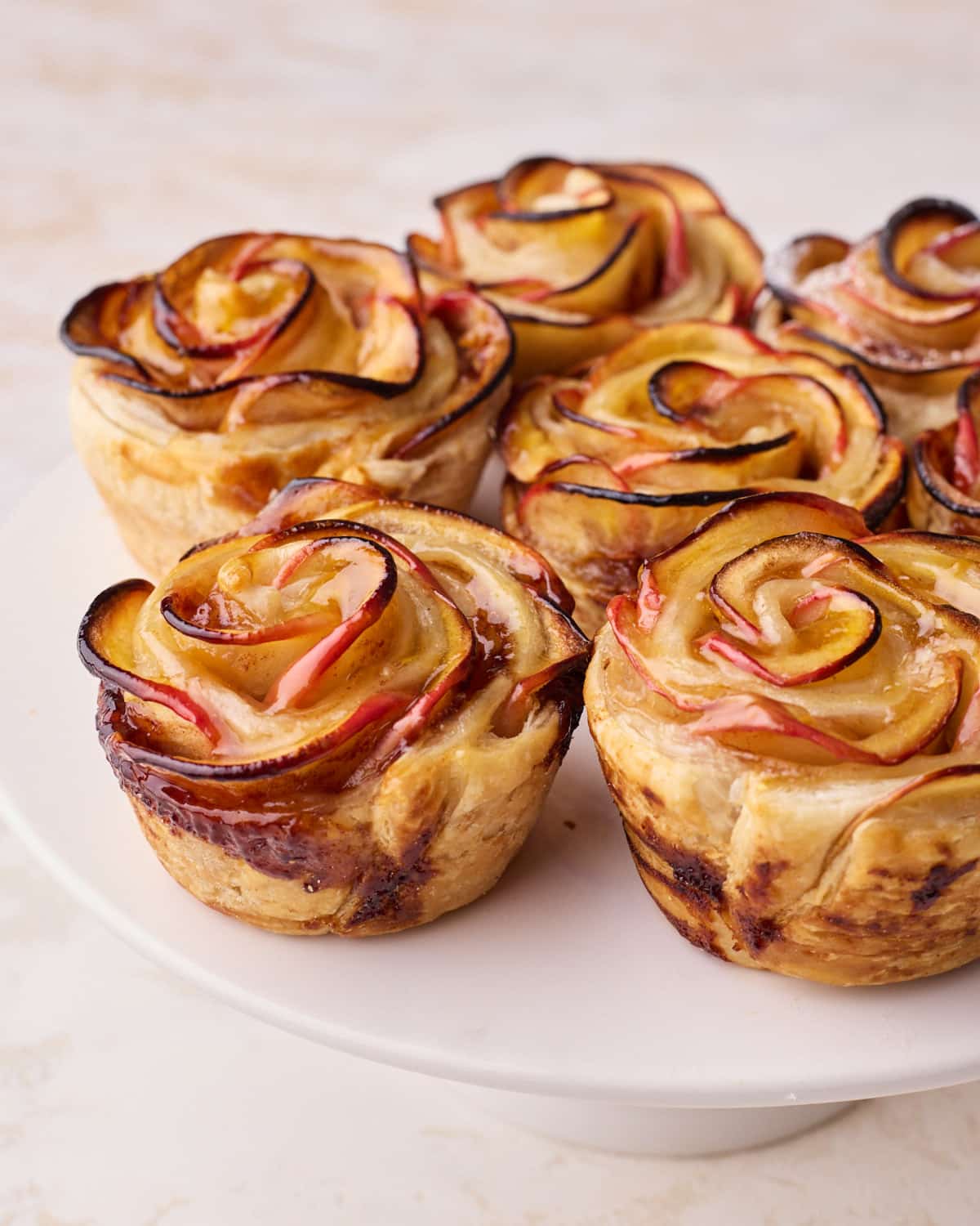 Apple roses baked in puff pastry, sitting on a cake stand.