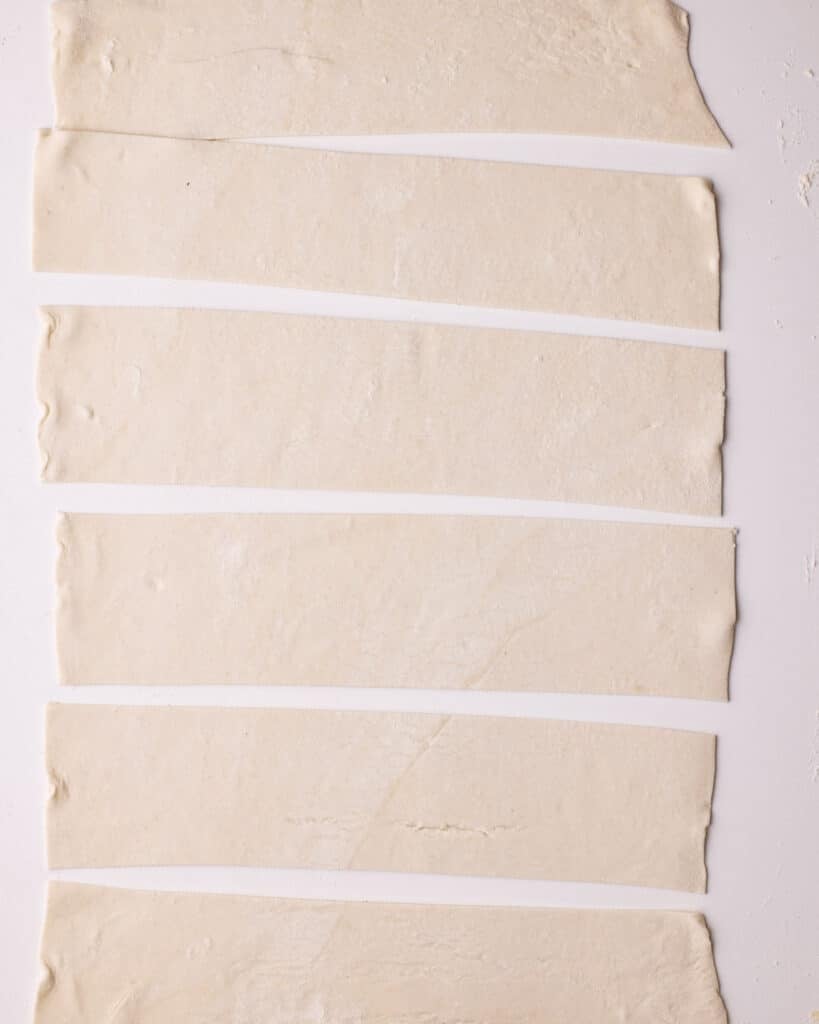 A sheet of rolled out puff pastry cut into six equal strips.