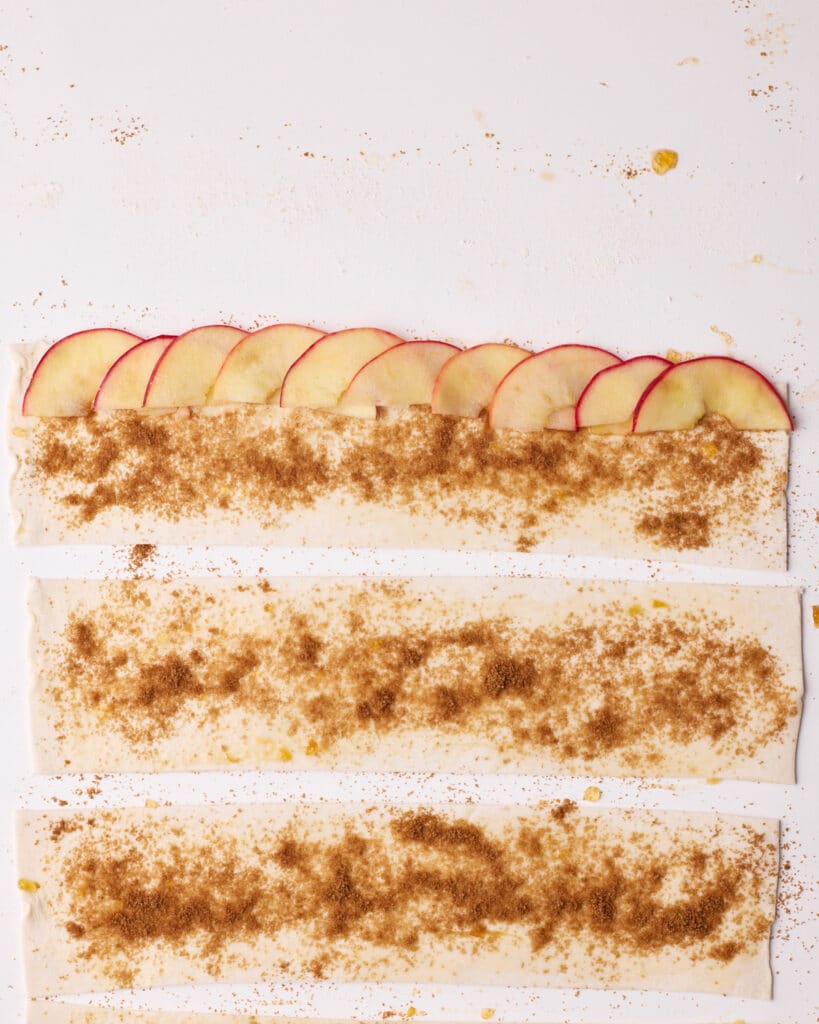 Process shot of placing thin slices of apple onto a strip of puff pastry to make apple roses.