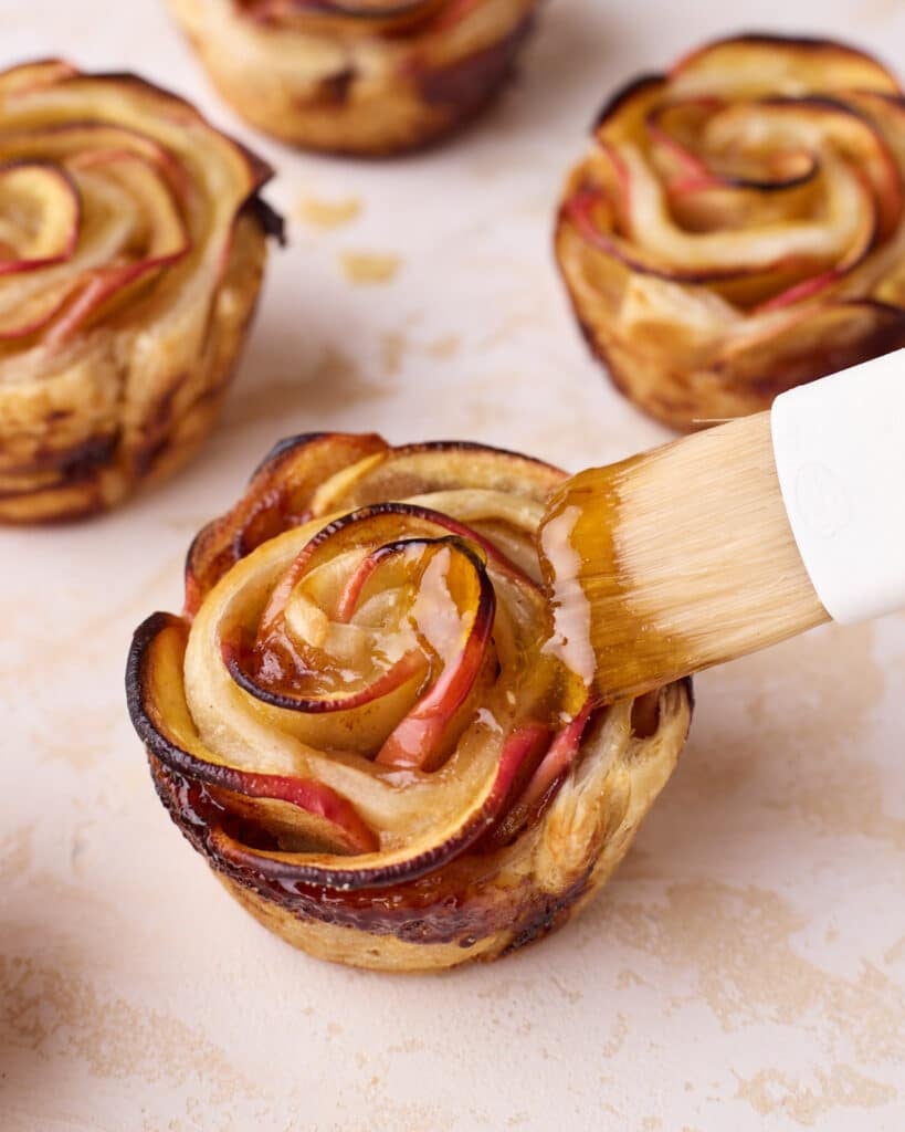 Brushing glaze made of melted apricot jam onto a baked apple rose.