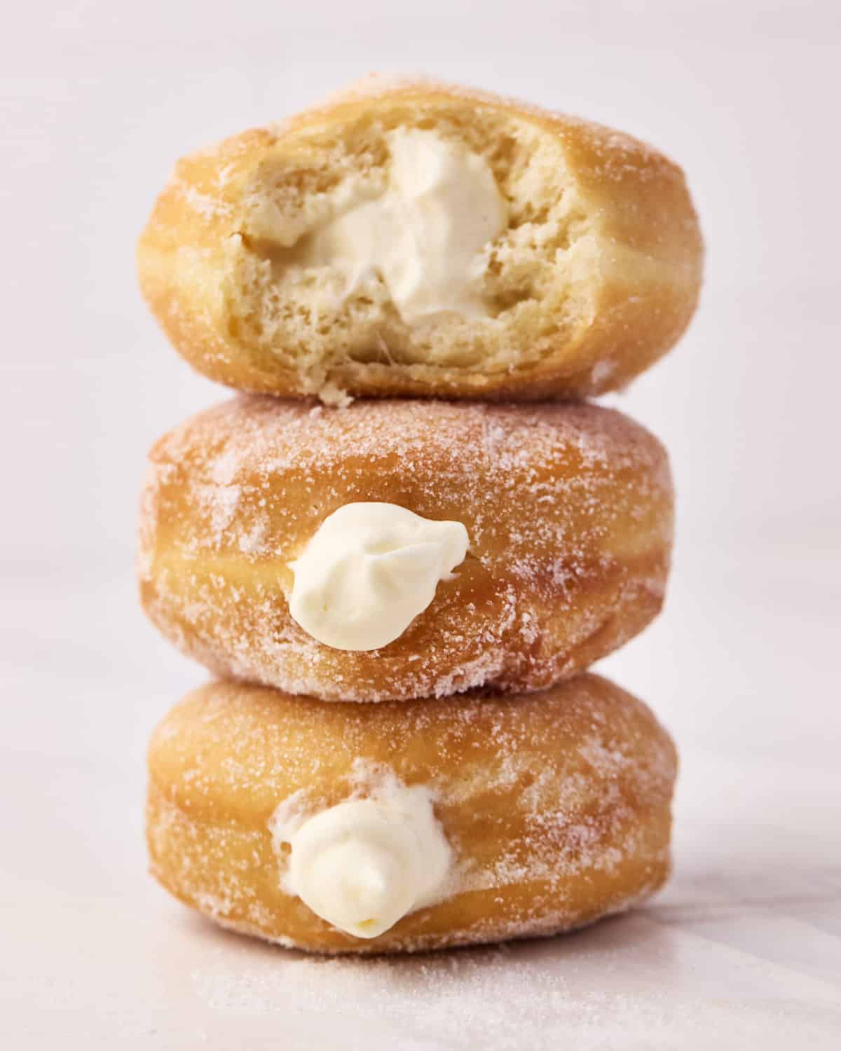 Three Bavarian cream donuts sitting in a stack, the top one has a bite taken out of it to reveal the creamy filling.