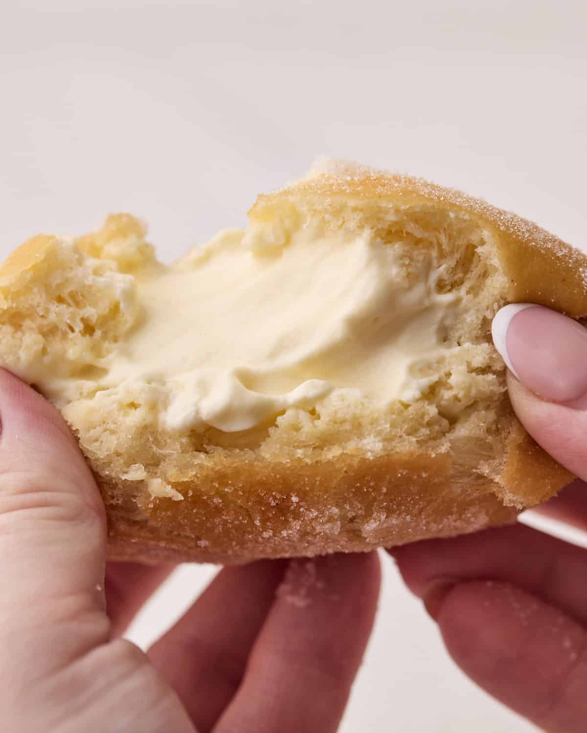 Bavarian cream donut being torn open to show an abundance of creamy filling inside. 