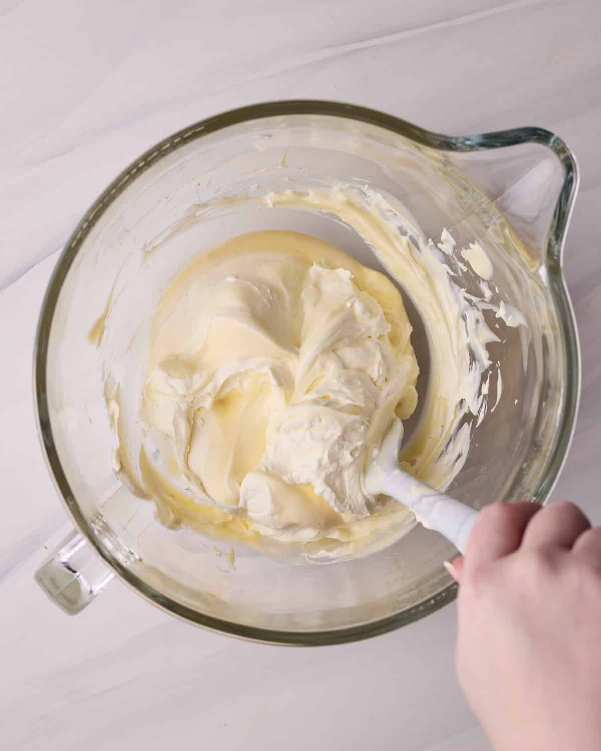 Whipped cream being folded into pastry cream with a rubber spatula to make creme legere - the filling inside Bavarian cream donuts.