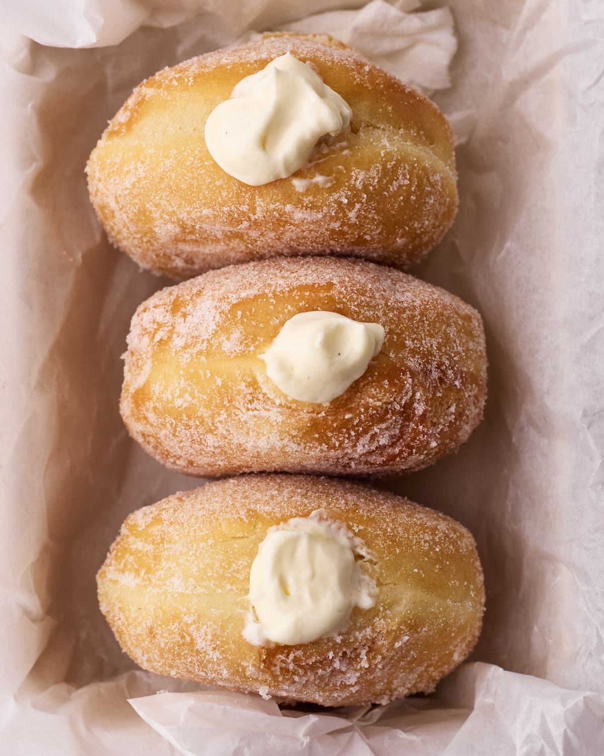 Three Bavarian cream donuts in a box with their creamy filling bulging out the front. 