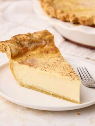 Slice of silky custard pie on a plate with the full pie in the background.