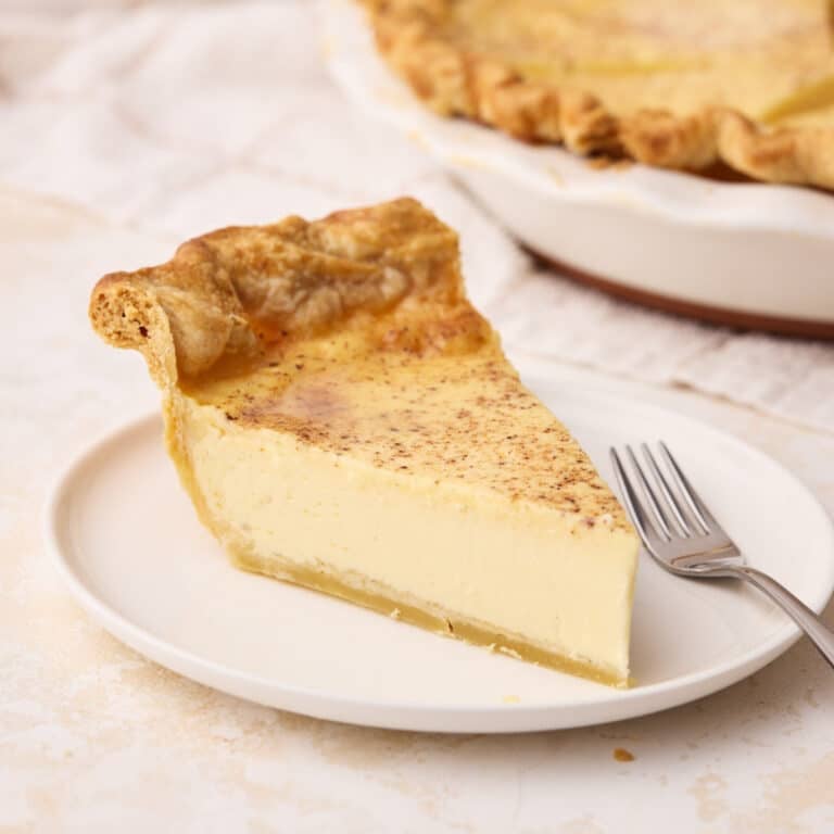 Slice of silky custard pie on a plate with the full pie in the background.