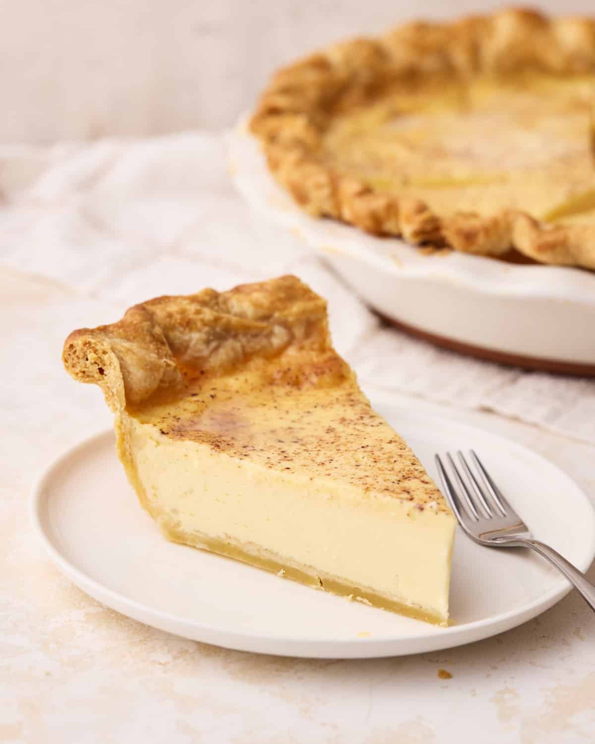 Slice of silky custard pie on a plate with the full pie in the background.