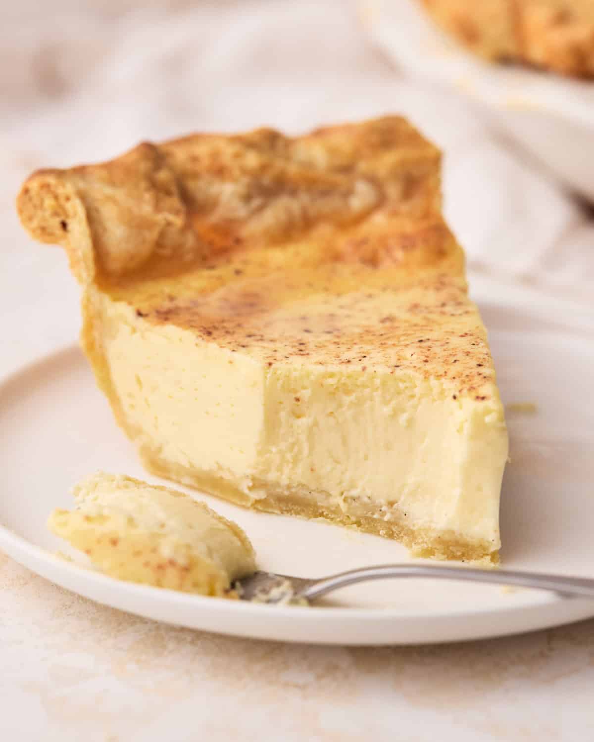 Slice of custard pie on a plate with a bite taken out to show the creamy texture. 