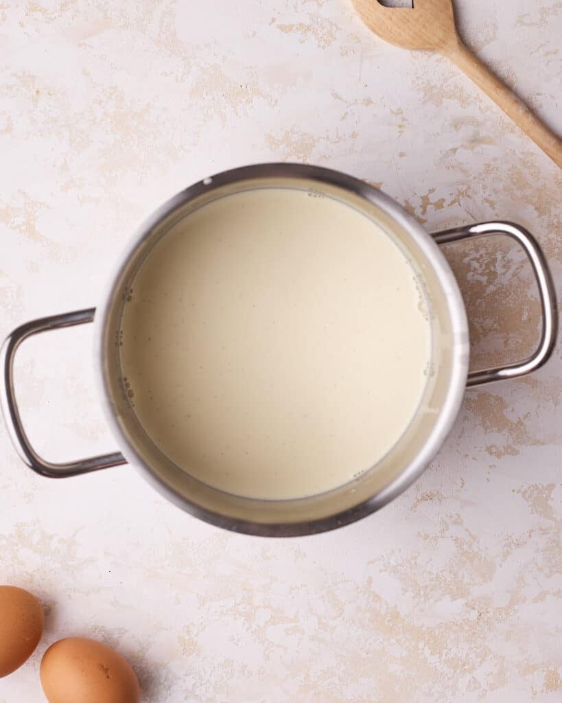 Scalding milk and heavy cream in a saucepan and infusing it with vanilla bean paste to make custard pie filling. 