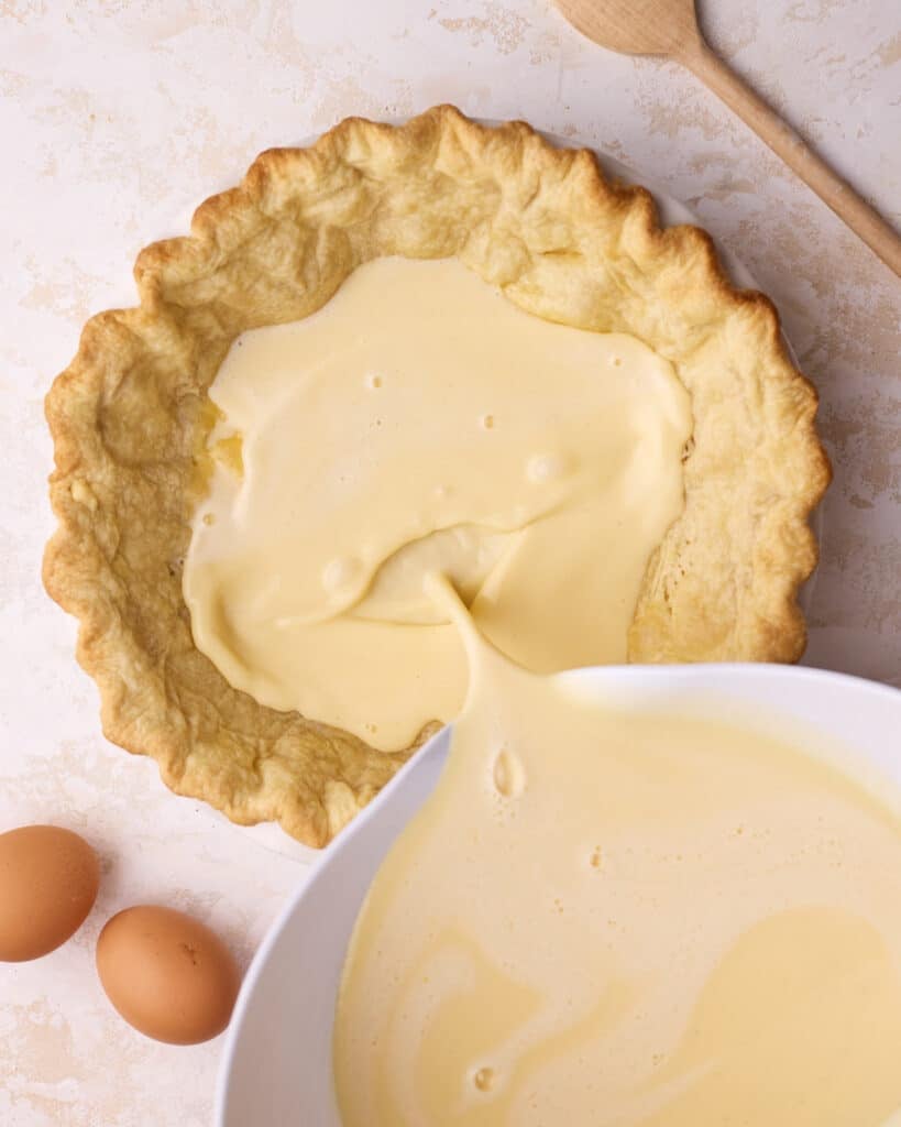 Pouring custard pie filling into a par-baked flaky pie crust to make custard pie. 