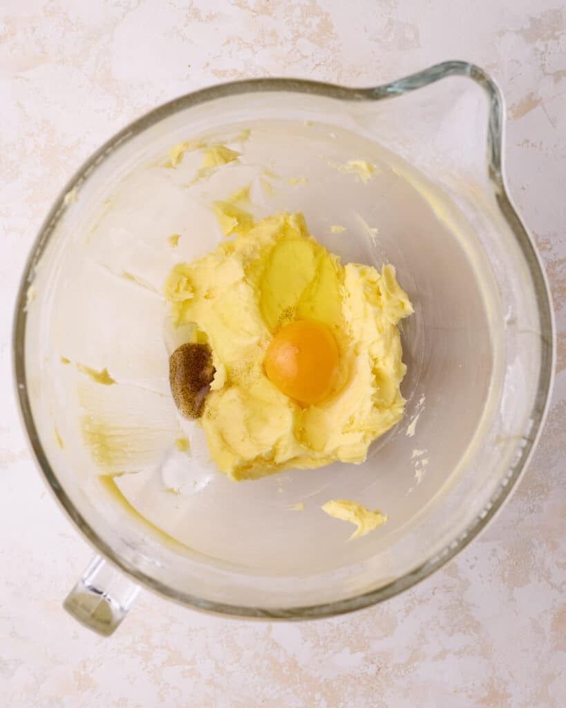 A mixer bowl showing egg and vanilla extract being added to the mixture for Danish butter cookies.