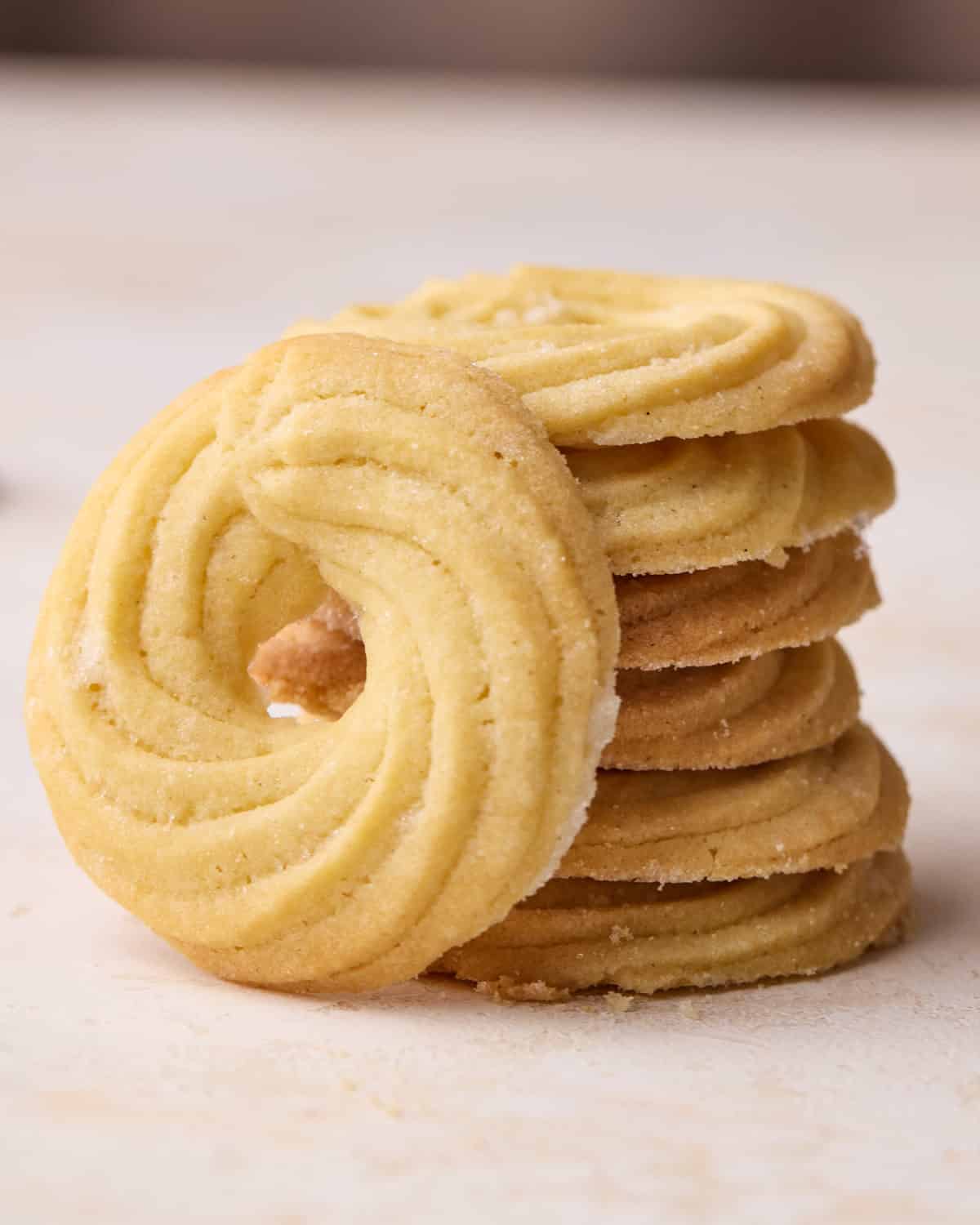 Stack of Danish butter cookies that have all been piped in a ring shape, one cookie is leaning on the side. 