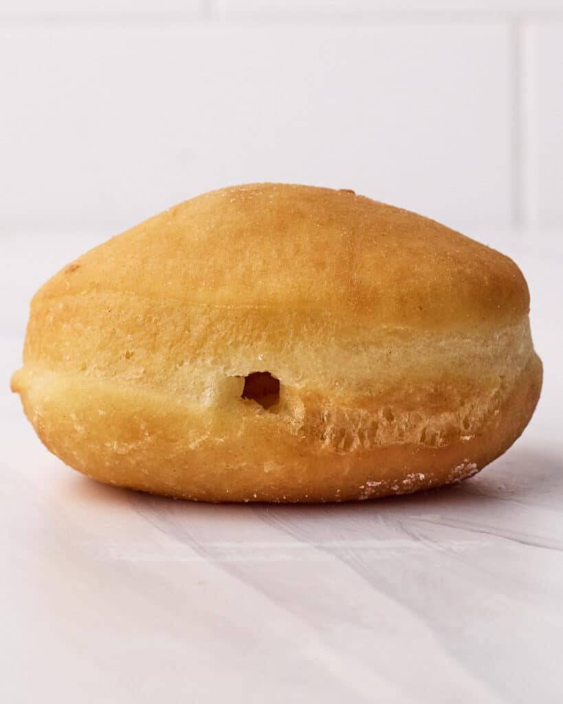 Close up of a homemade donut with a hole poked in the side to make room for filling to turn it into a Boston cream donut.