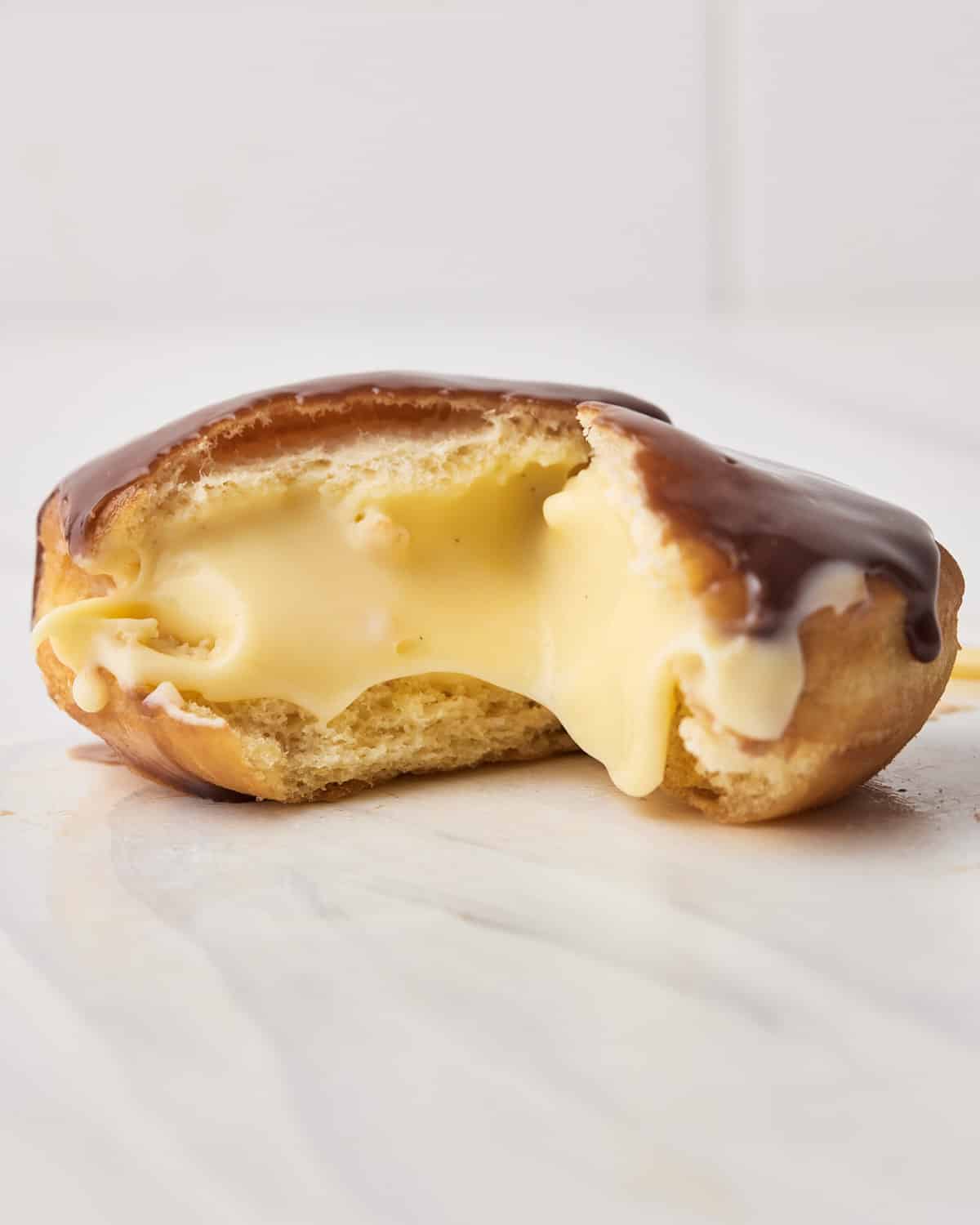 Boston cream donut that has been ripped open and all the custard filling is oozing out. 