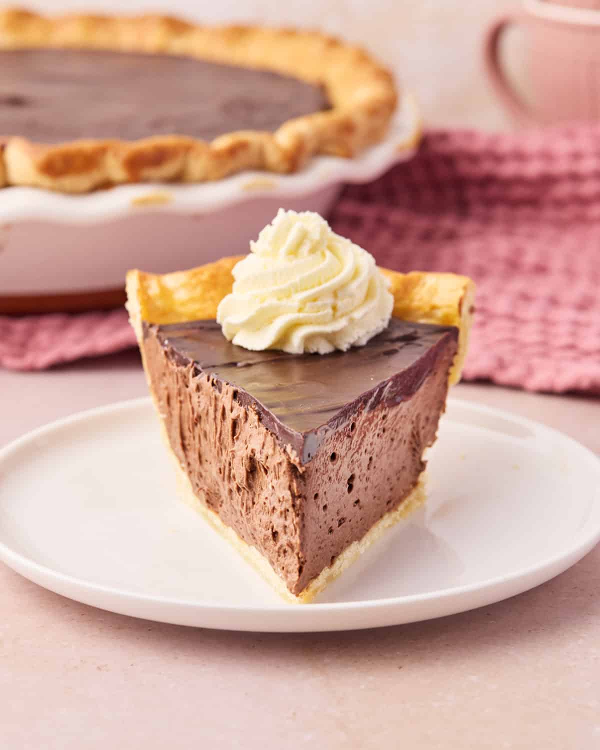 Slice of chocolate mousse pie in a homemade pie crust, pointing to the camera with whipped cream on top.