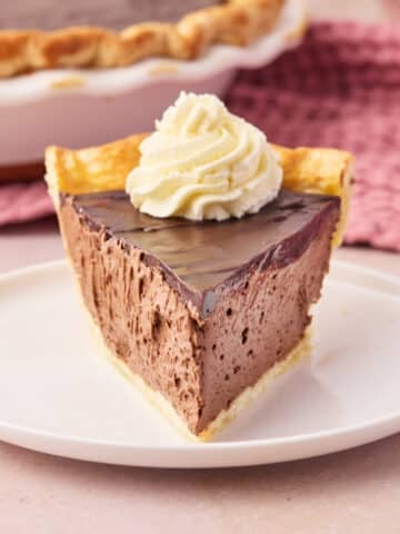 Slice of chocolate mousse pie in a homemade pie crust, pointing to the camera with whipped cream on top.