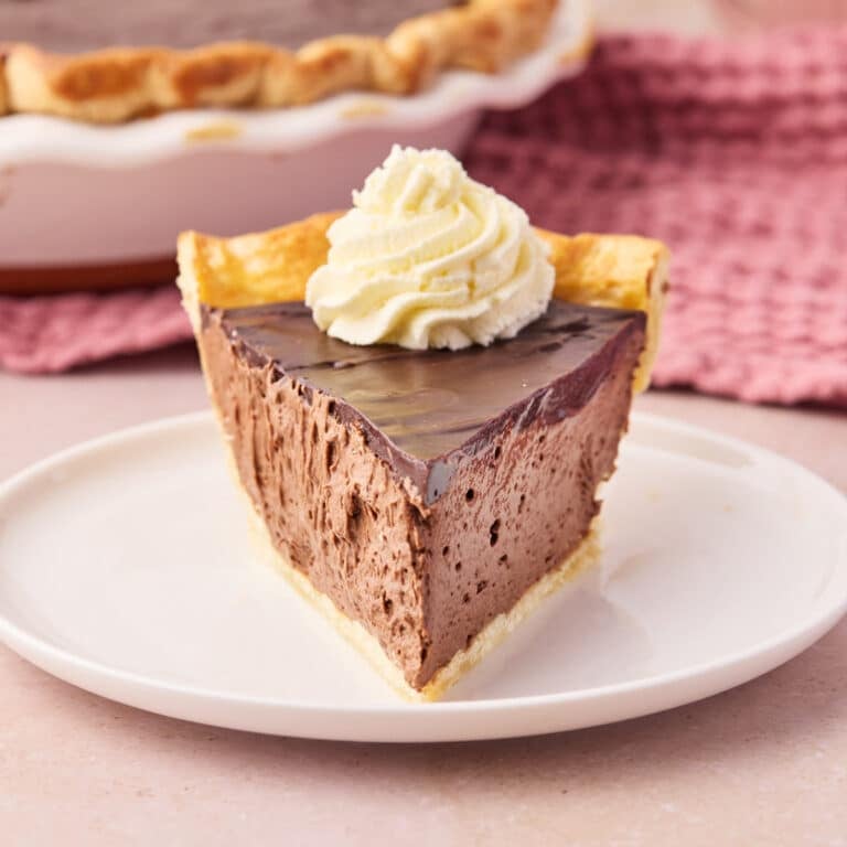 Slice of chocolate mousse pie in a homemade pie crust, pointing to the camera with whipped cream on top.