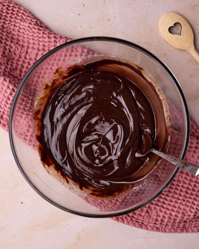 Chocolate ganache in a glass bowl on a pink towel.