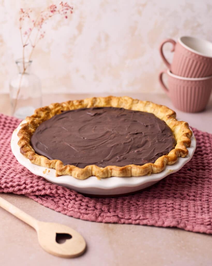 Chocolate mousse pie in a flaky pie crust, sitting in a pie dish on a pink kitchen towel. 