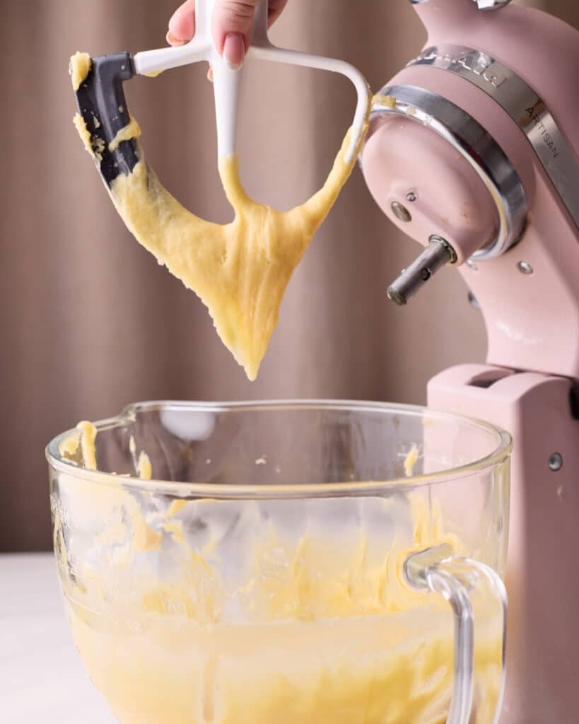 A stand mixer paddle attachment with choux pastry hanging from it in a 'V' shape, this is the 'v test' to check if choux pastry is ready to be used. 