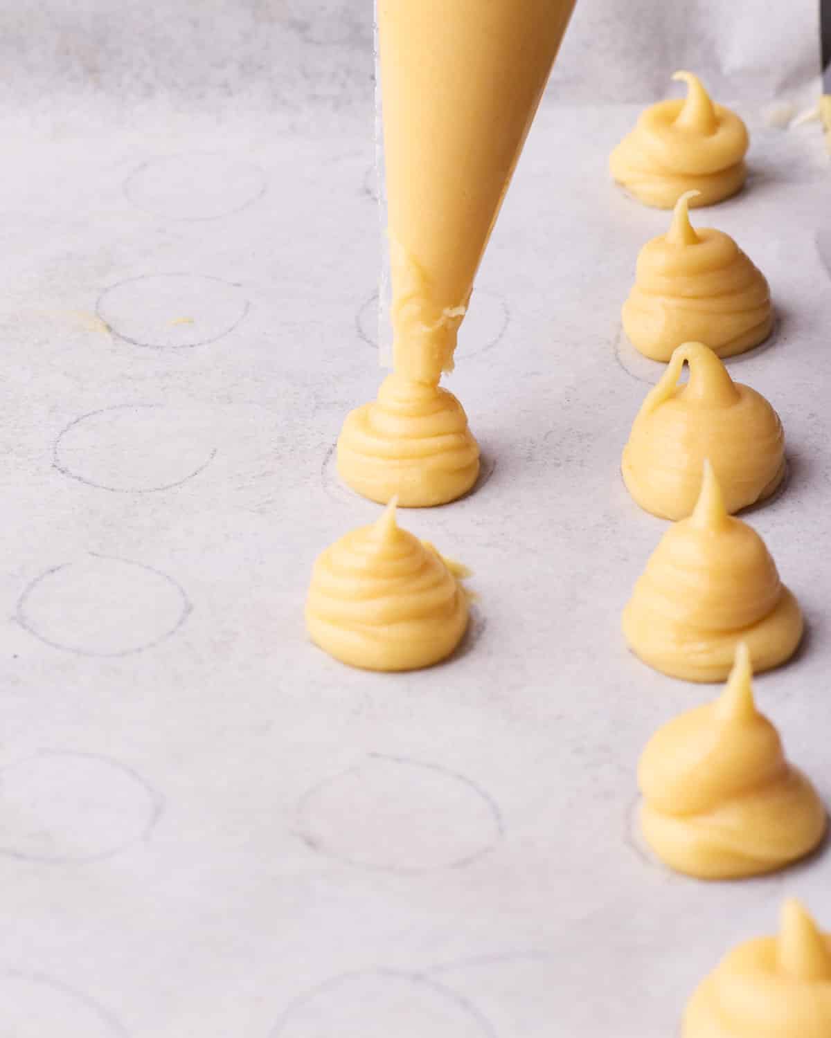Piping choux pastry onto a baking sheet into small mounds to make profiteroles.