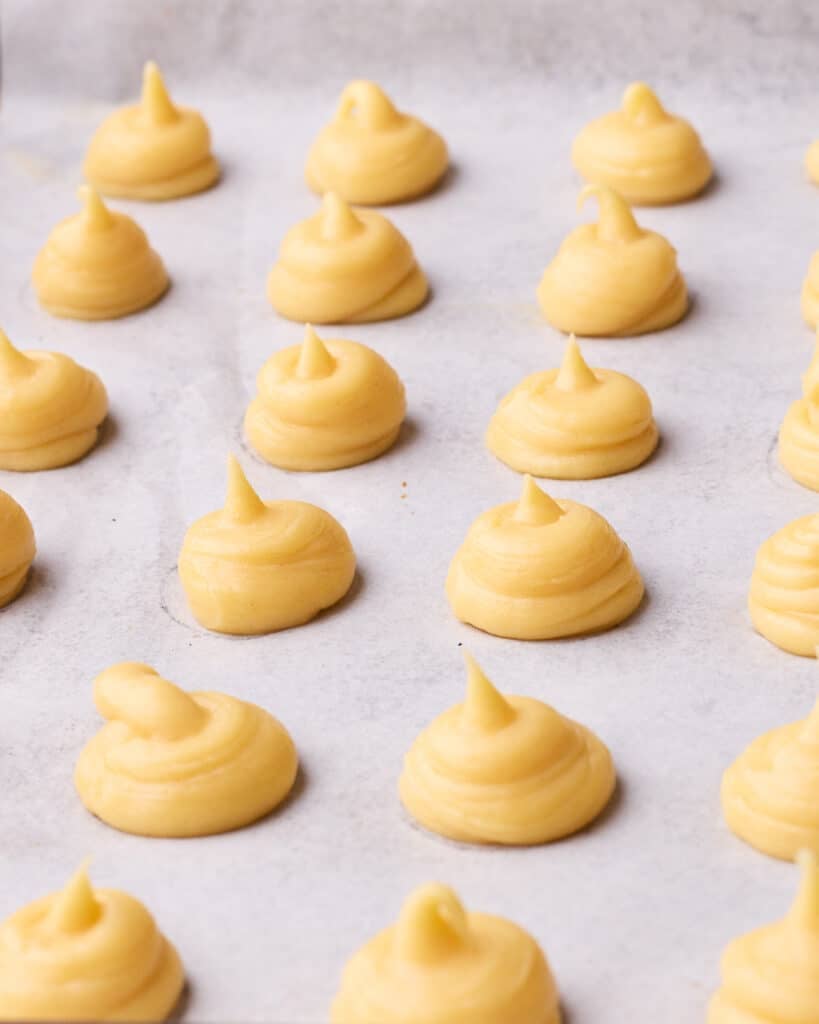 Little domes of piped choux pastry on a baking sheet to make profiteroles. 