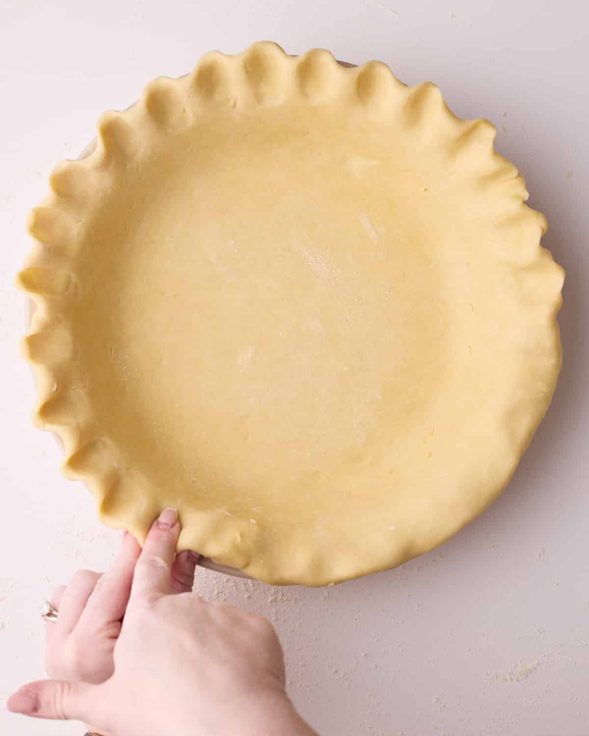 Process shot showing how to crimp pie crust using the scallop method, pinching the dough between forefinger and thumb and pressing with the finger on the other hand. 