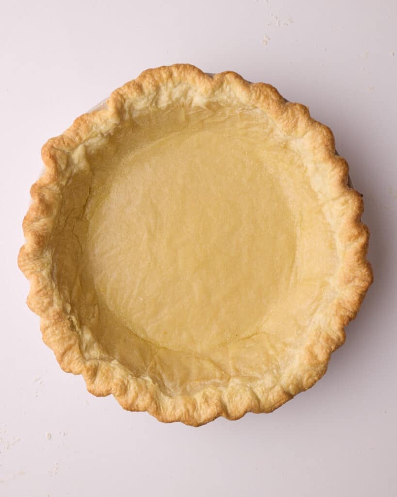 Flaky pie crust after it has been partially blind baked and the pie weights have been removed - the edges are lightly golden brown but the bottom is not yet baked. 