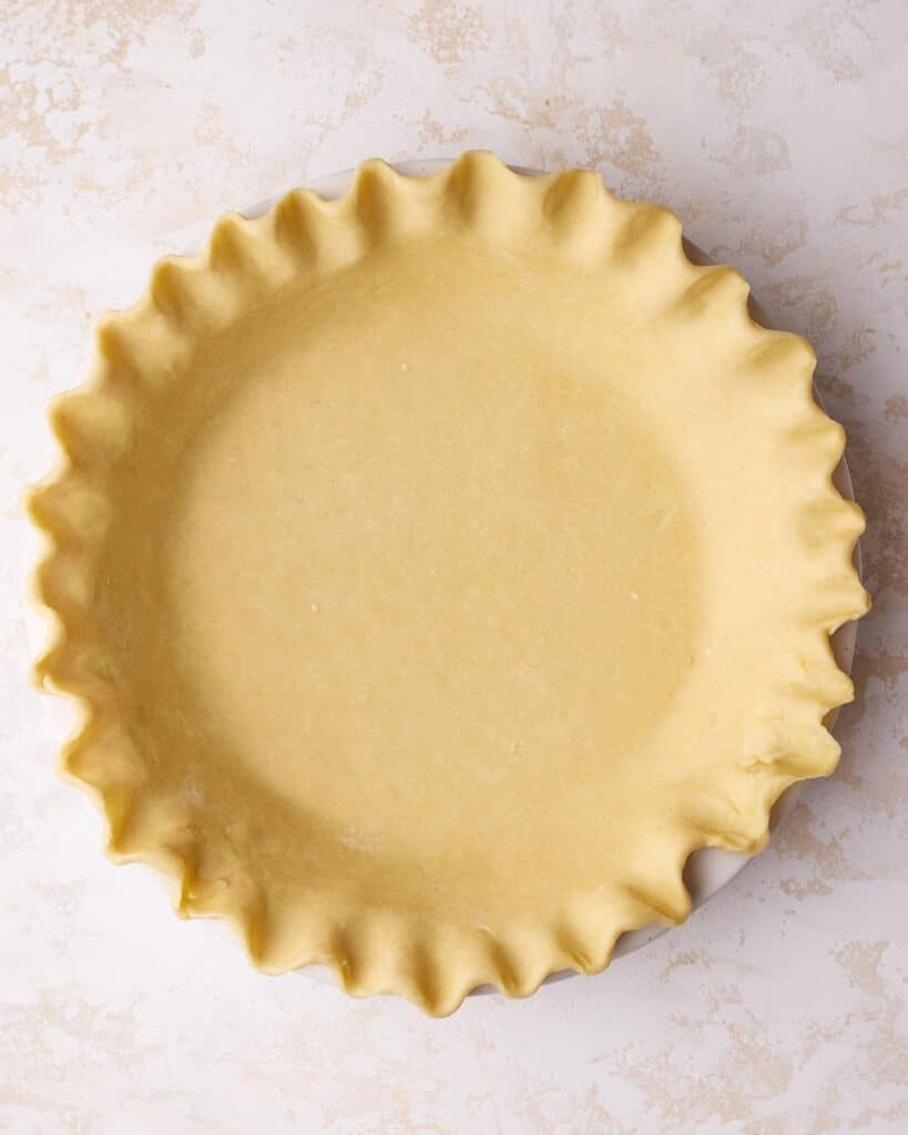 Homemade pie crust, unbaked in a pie dish with crimped edges.