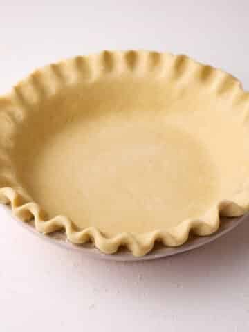 Homemade pie crust, unbaked in a pie dish with crimped edges.