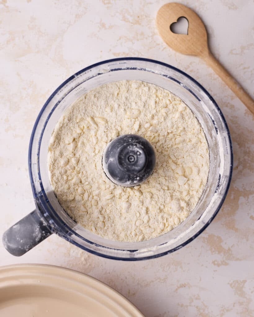 Process of making homemade pie dough, showing the butter being pulsed down to pea-sized chunks in the flour. 