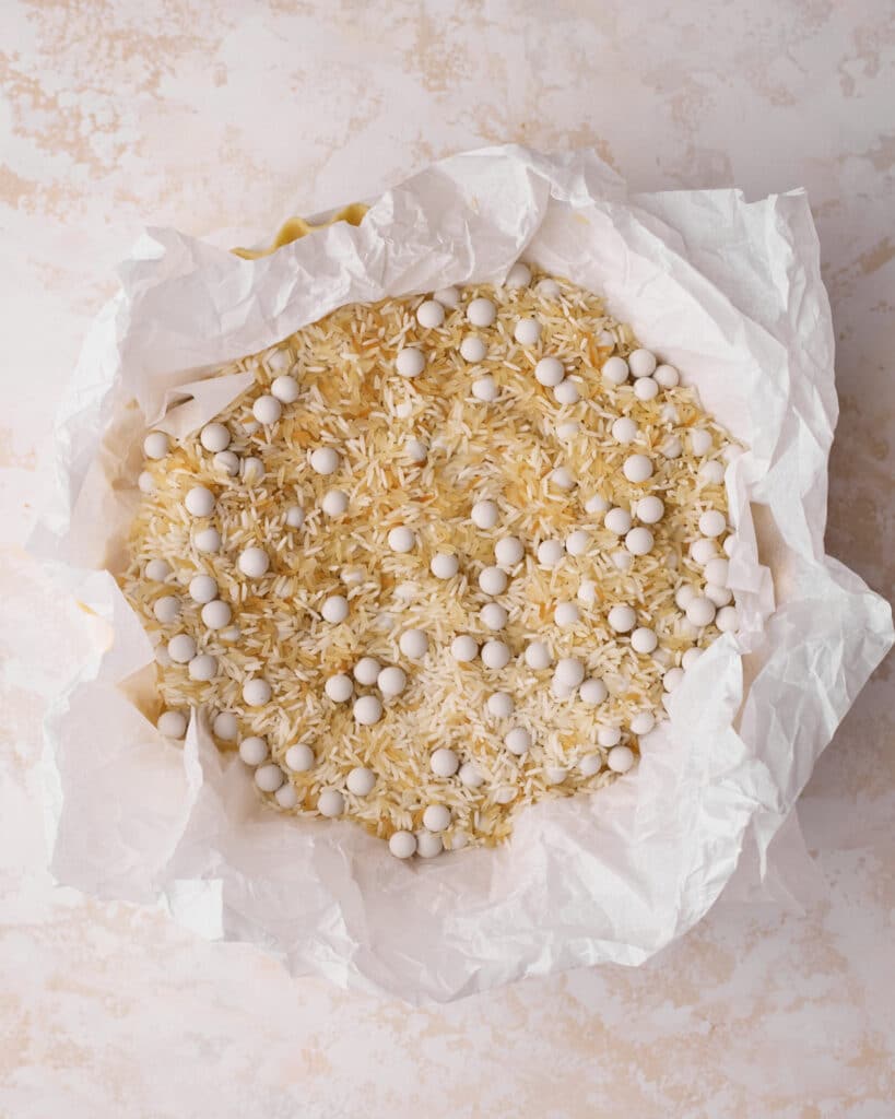 Pie weights and rice on top of parchment paper in a pie crust, ready to be blind baked.