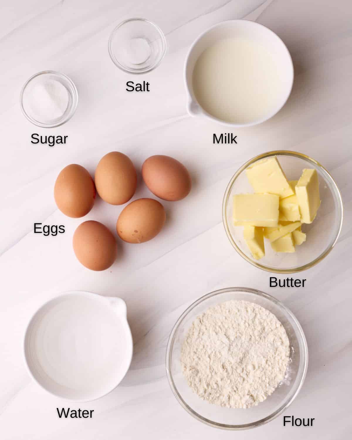 Ingredients to make choux pastry, including eggs, butter, flour, sugar, salt, milk and water. 