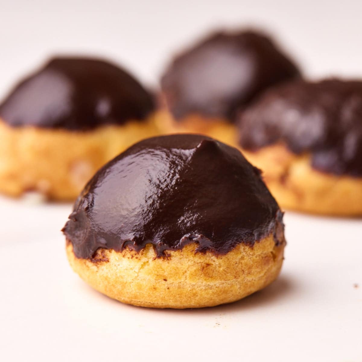 Four profiteroles on a white table with shiny chocolate glaze and perfect round shape.