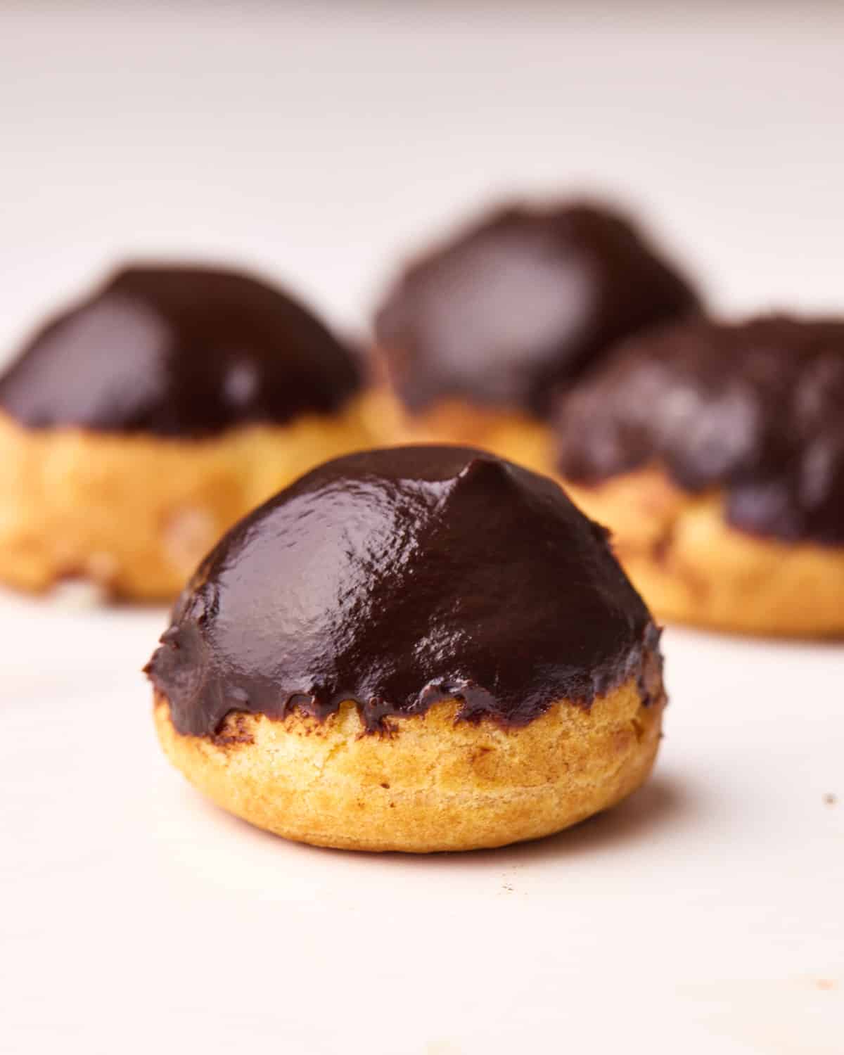 Four profiteroles on a white table with shiny chocolate glaze and perfect round shape.